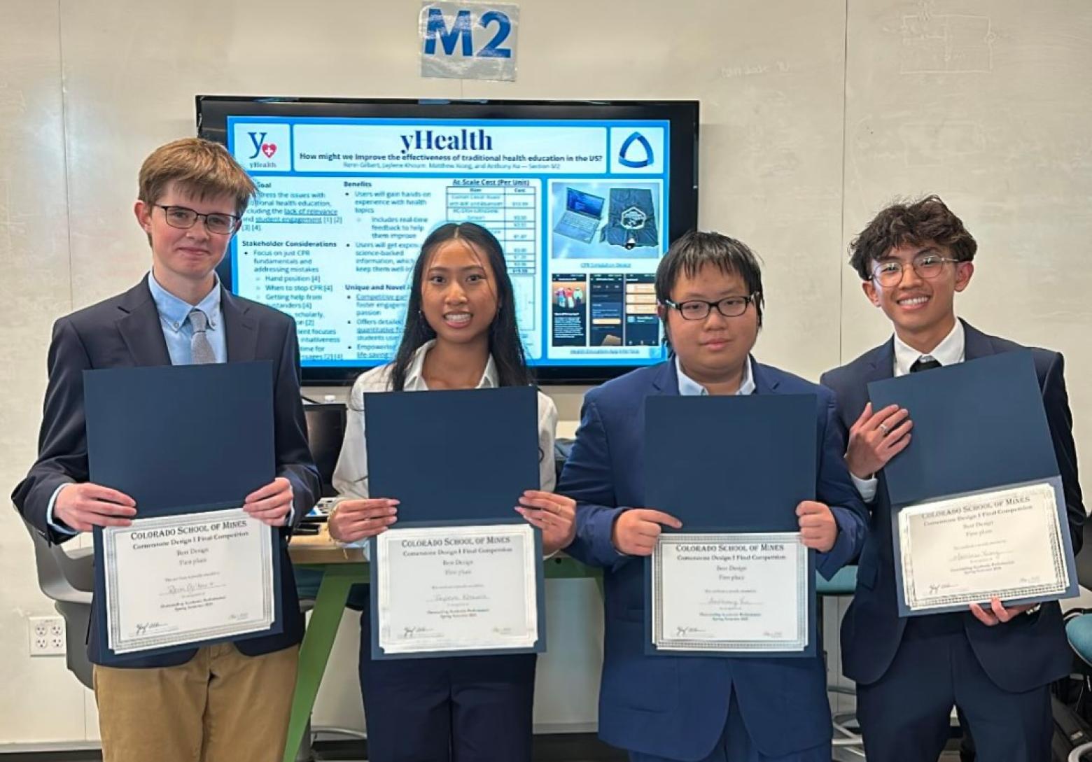 Four students standing in front of digital poster hold award certificates