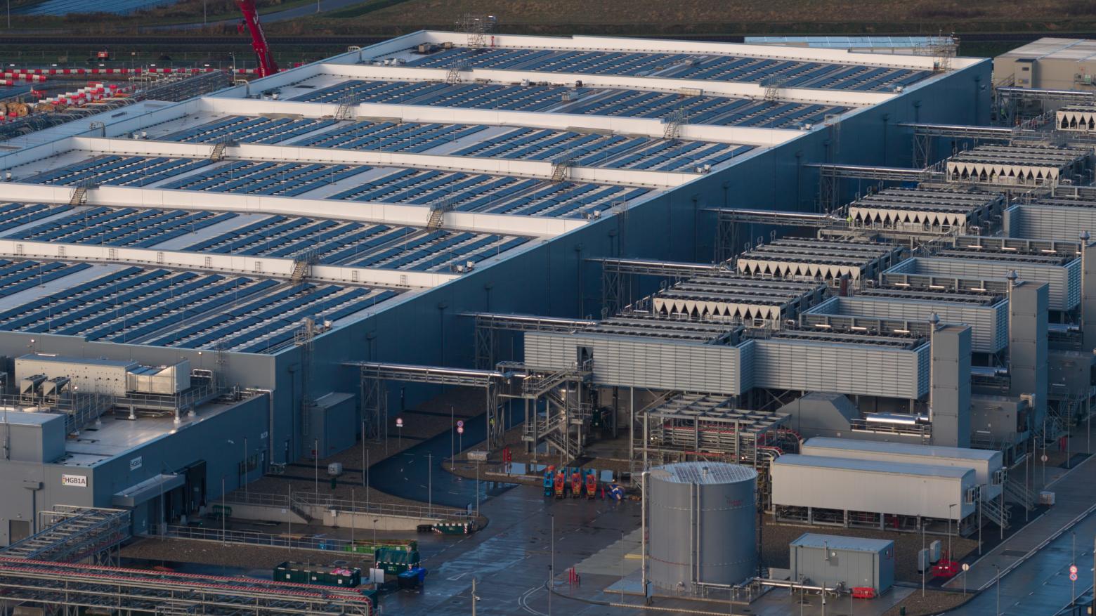 Aerial view of a massive, modern data center featuring a roof covered in solar panels and extensive cooling infrastructure on the side.