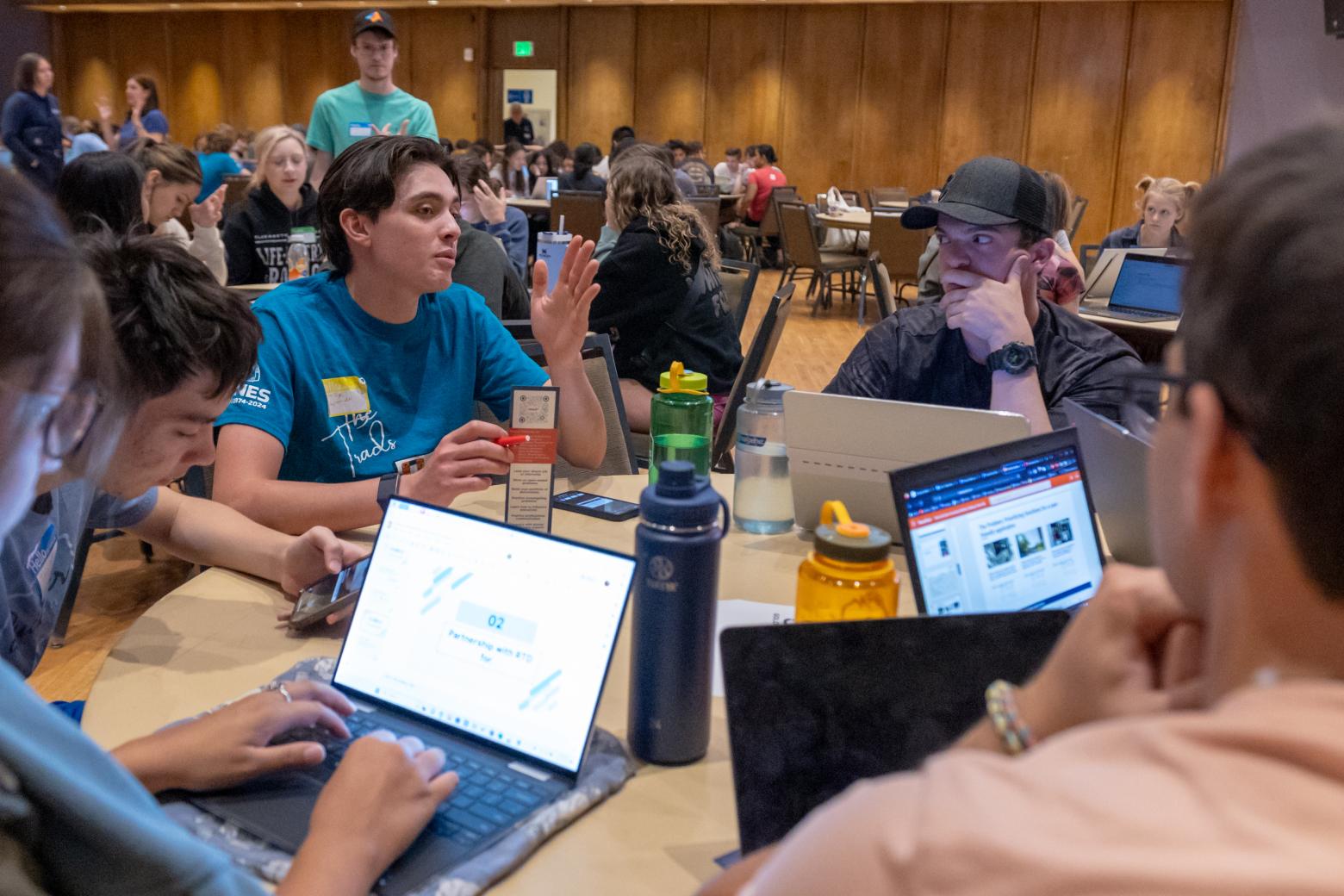 Mines students sit around a table with laptops discussing the Hearts and Gears Innovating Mobility Challenge.