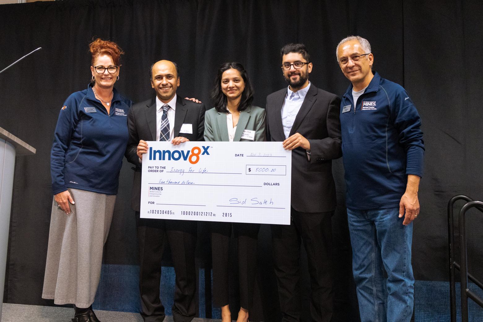Mines student and faculty winners stand on stage at the GEFI Innov8x Challenge holding an honorary check for 5000 dollars.