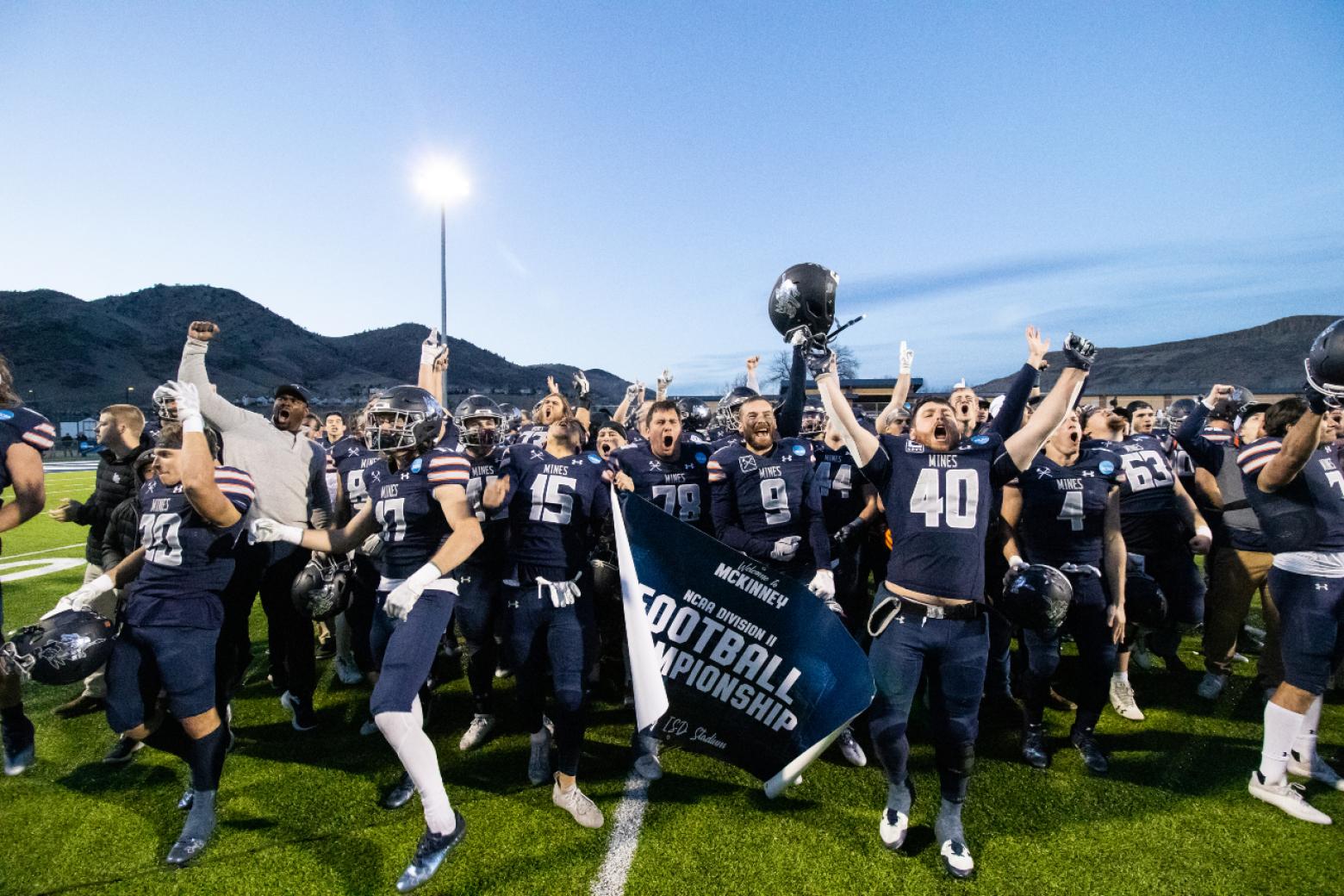 Mines football team celebrates on field with a NCAA DII banner