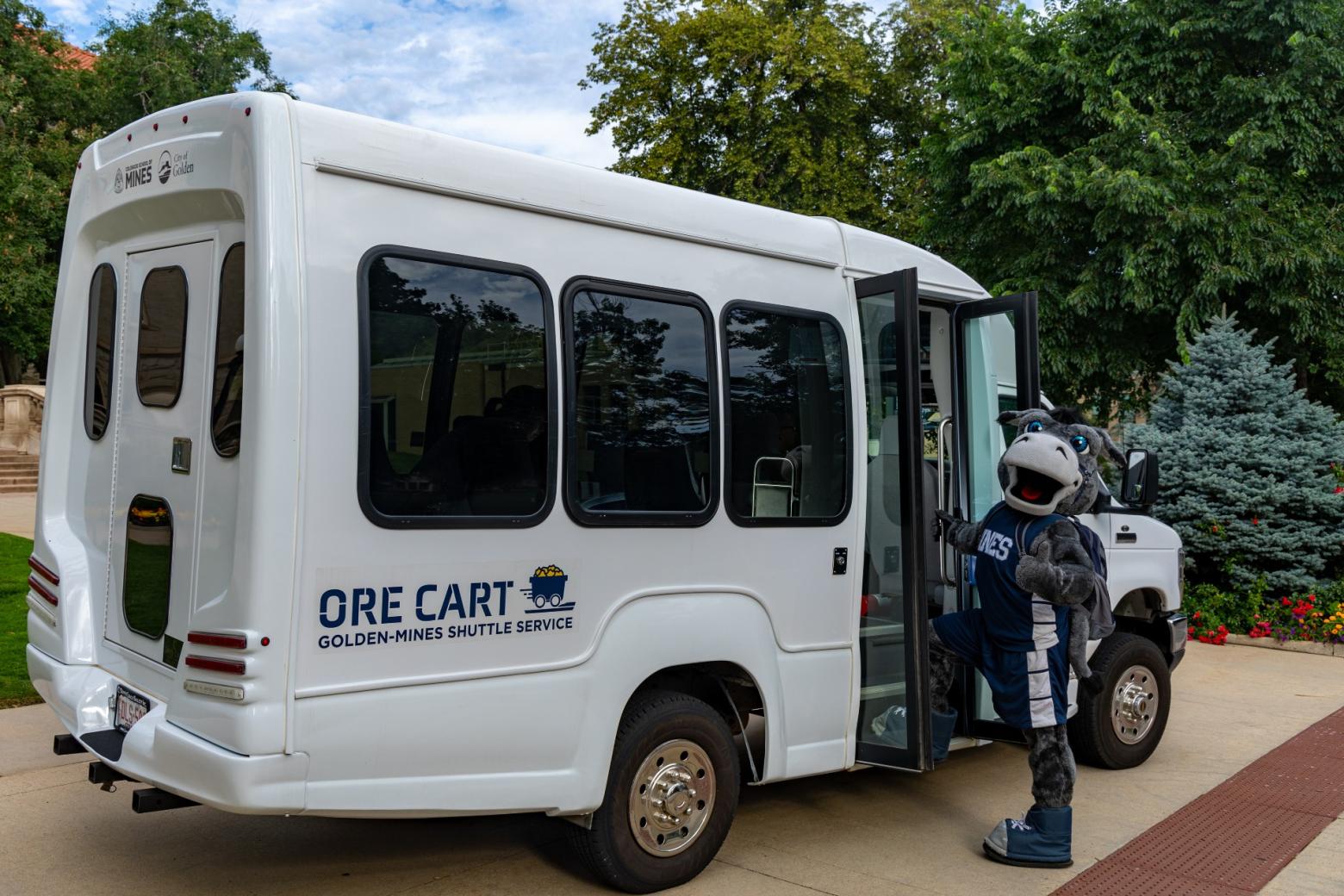 Colorado School of Mines mascot stands in front of a Mines Orecart shuttle bus