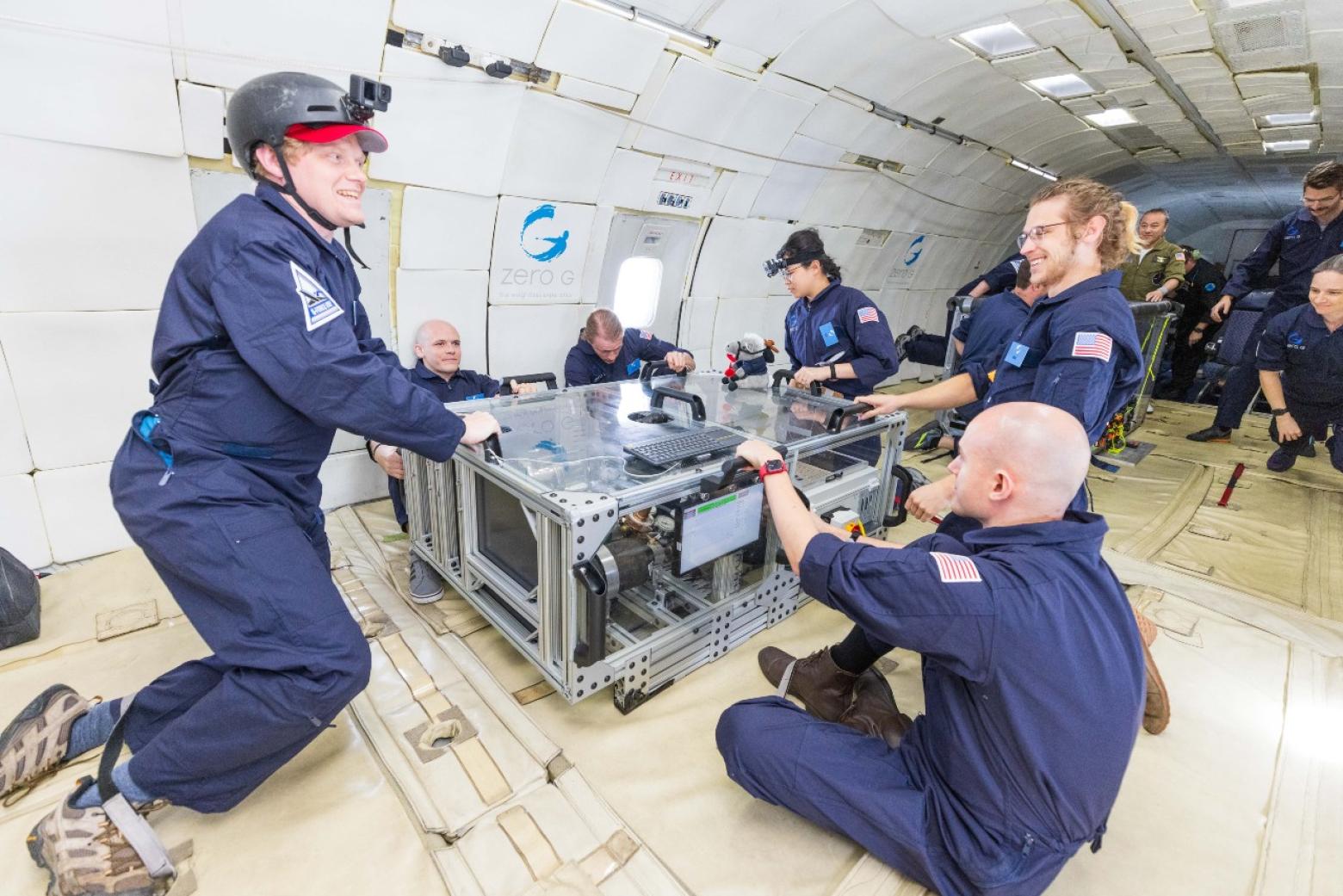 A group of people in blue flight suits conduct experiments during a parabolic flight