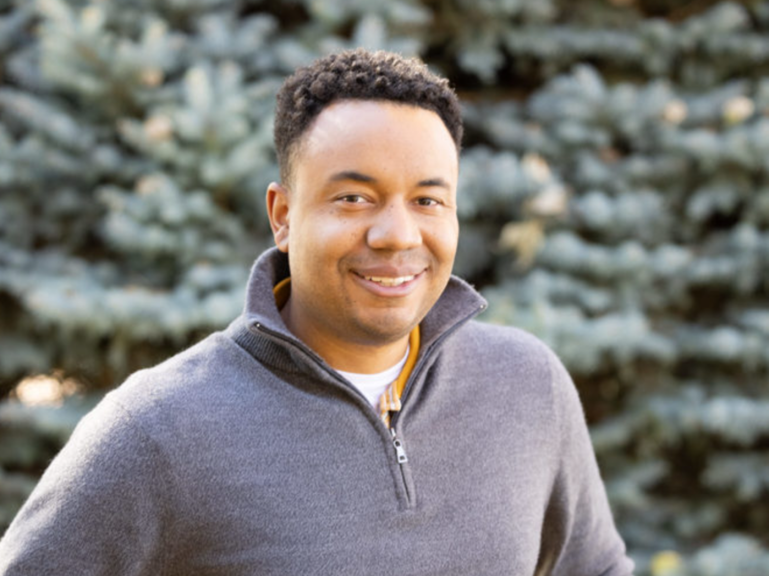 Profile photo of Joshue Dickerson standing in front of evergreen trees.