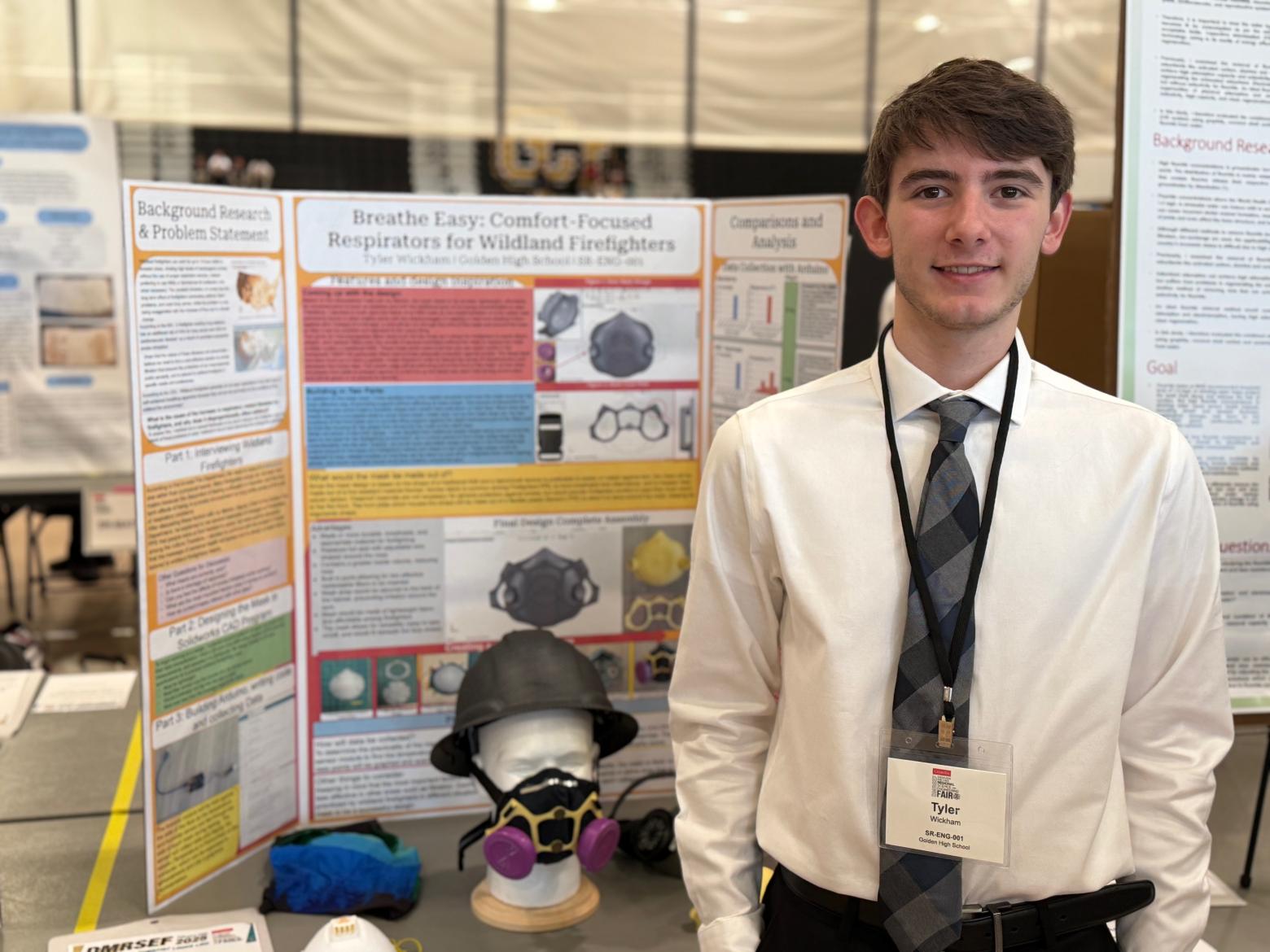 Tyler Wickham stands in front of a science fair poster wearing white shirt and tie