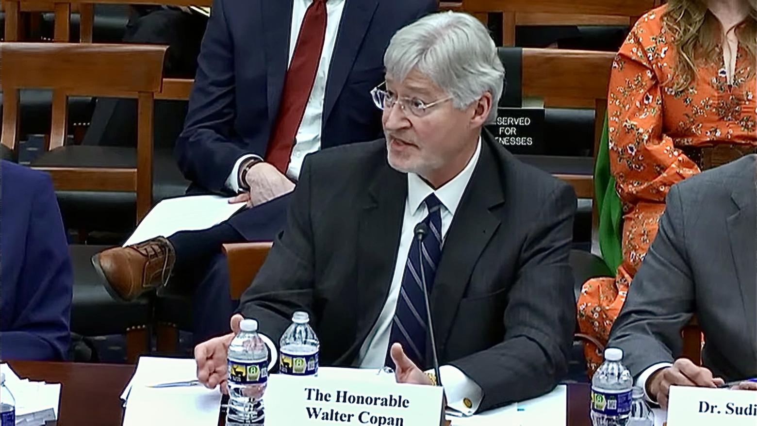Walt Copan sits at a table behind his name plate