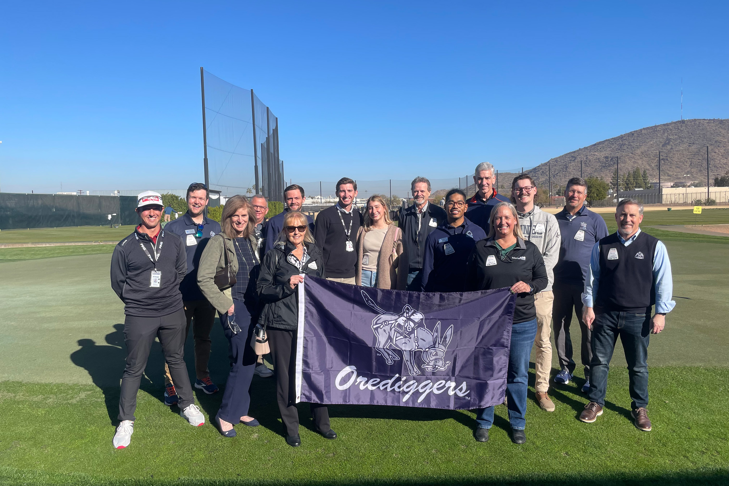 A group of Mines alumni hold an Oredigger flag on the PING Golf campus