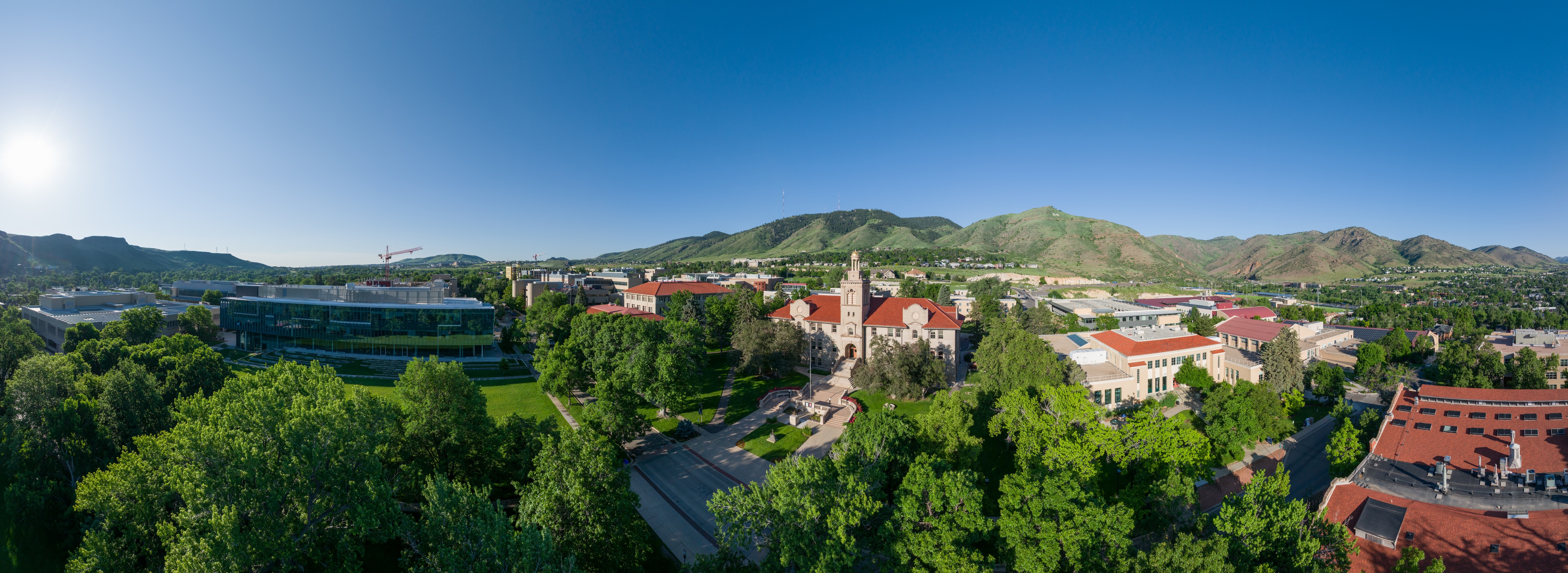 Panoramic view of Mines with buildings, green trees, and mountains under a clear blue sky