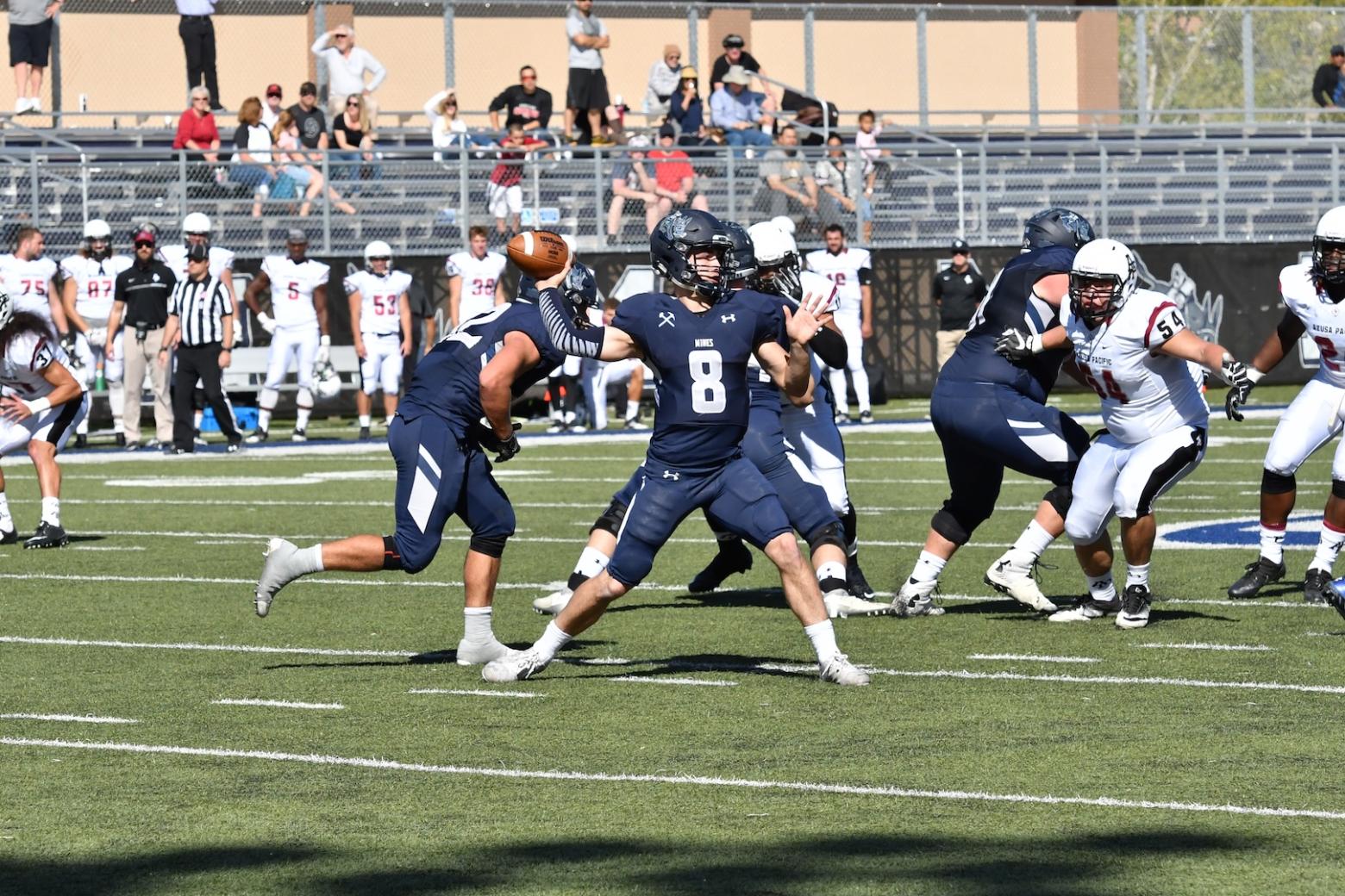 Justin Dvorak about to throw a football with other football players surrounding him.