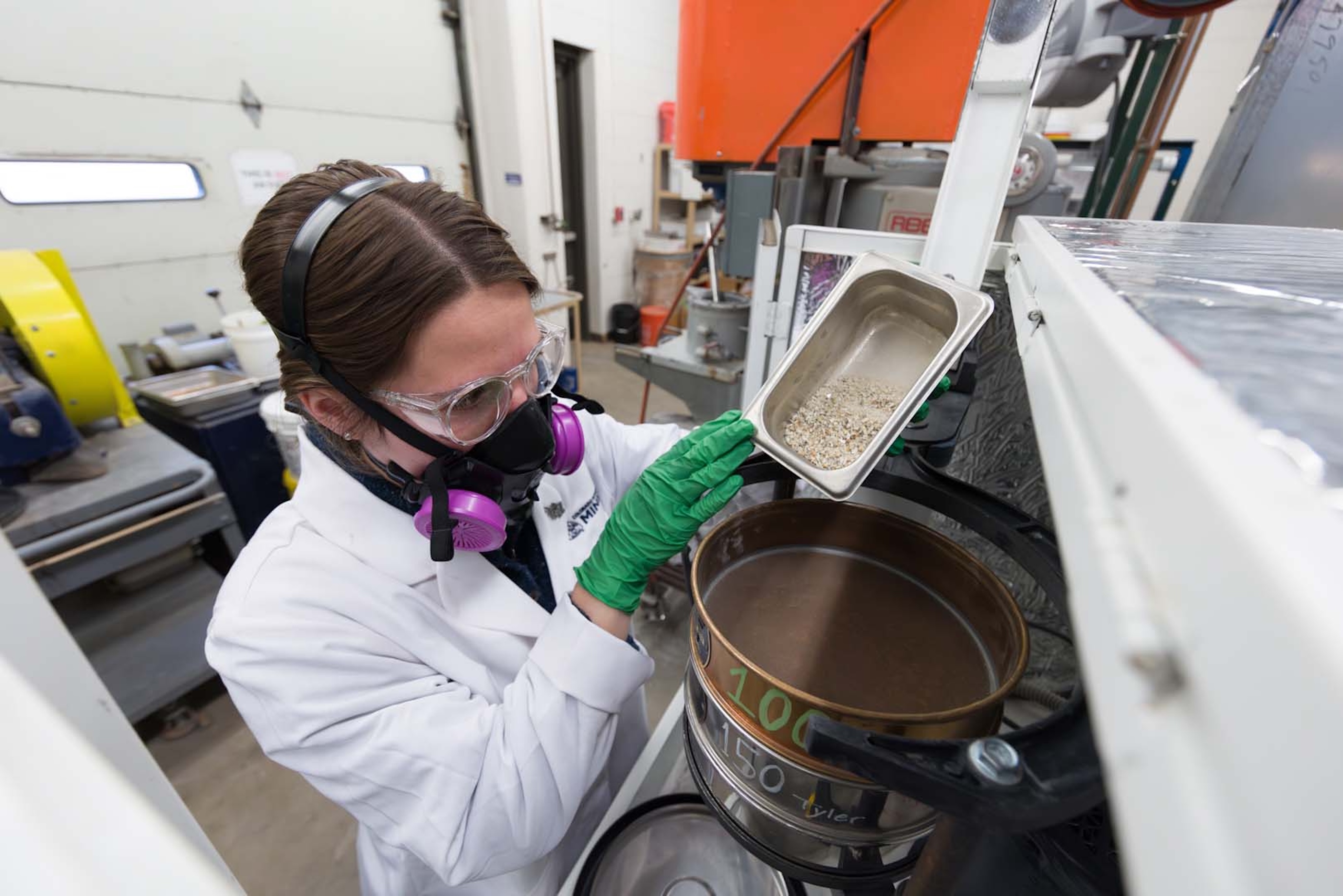 Student wearing a respirator in a lab pouring a sample into a RO-tap machine.