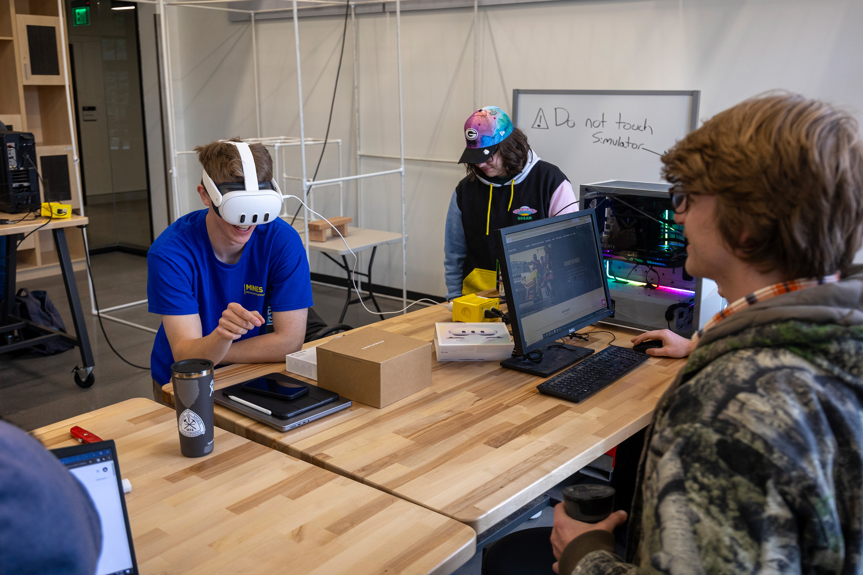 A student wearing a VR headset works on a project with two other students