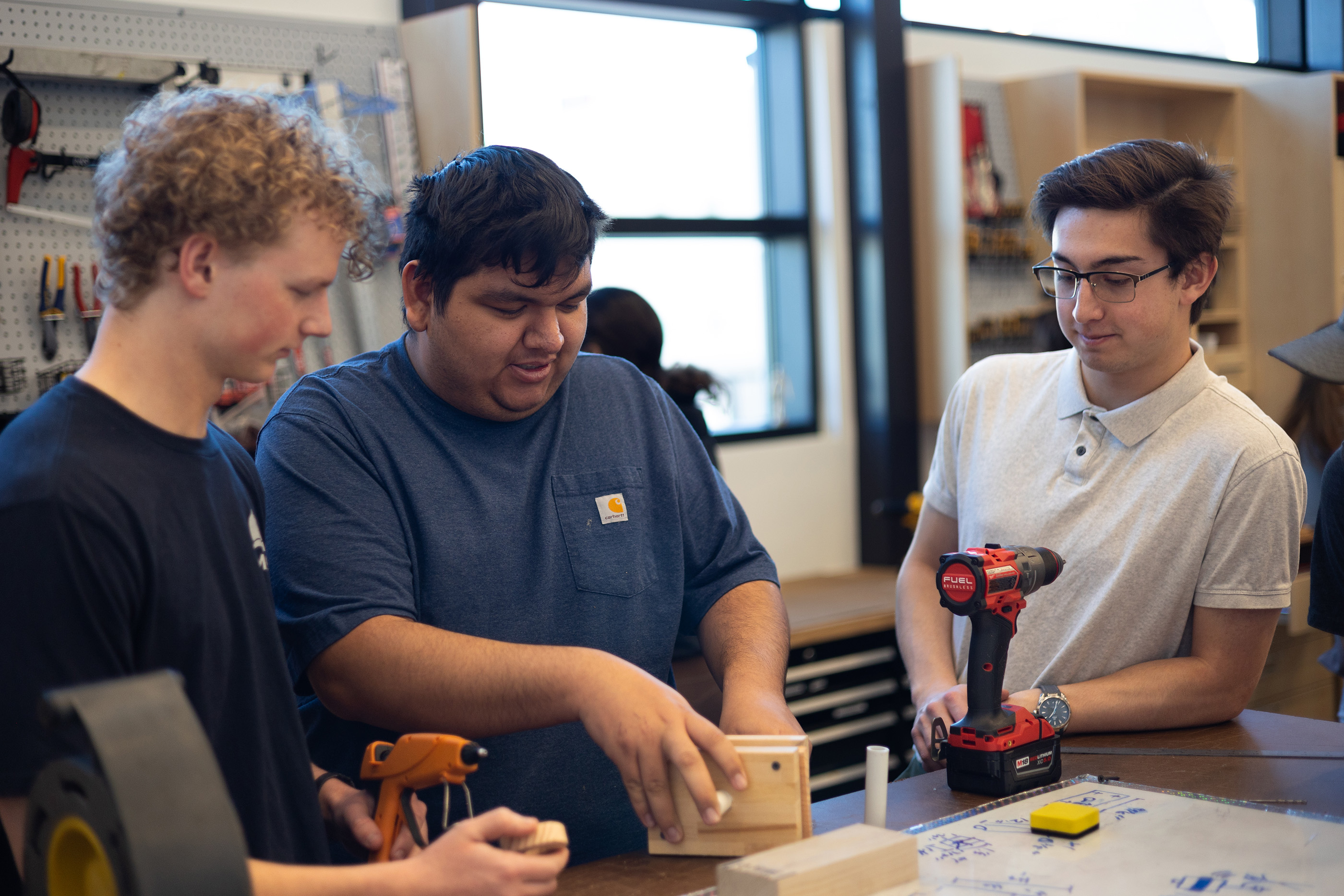 Three students build a physical model with wood and PVC