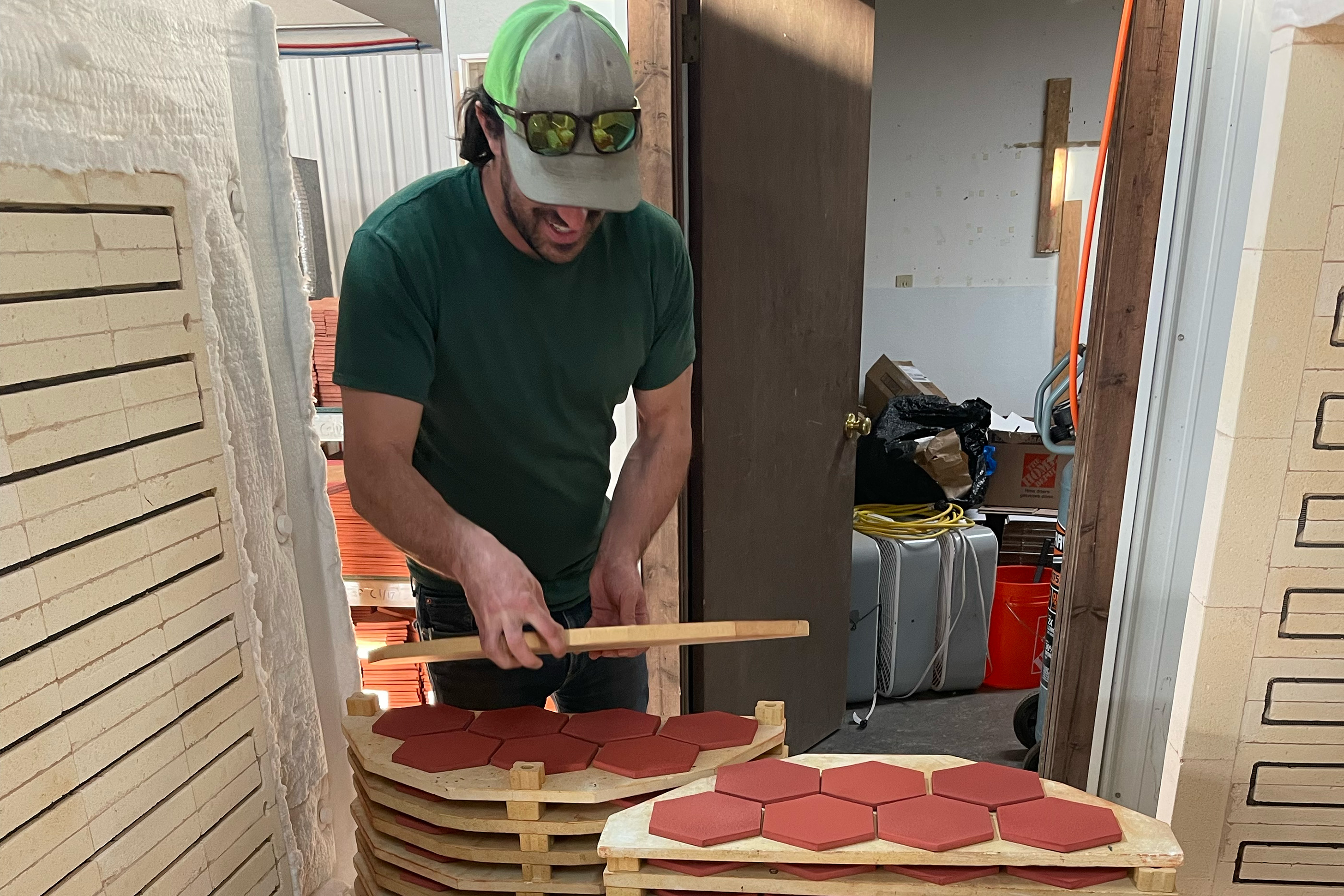 A man wearing a baseball cap loads clay tiles into a kiln