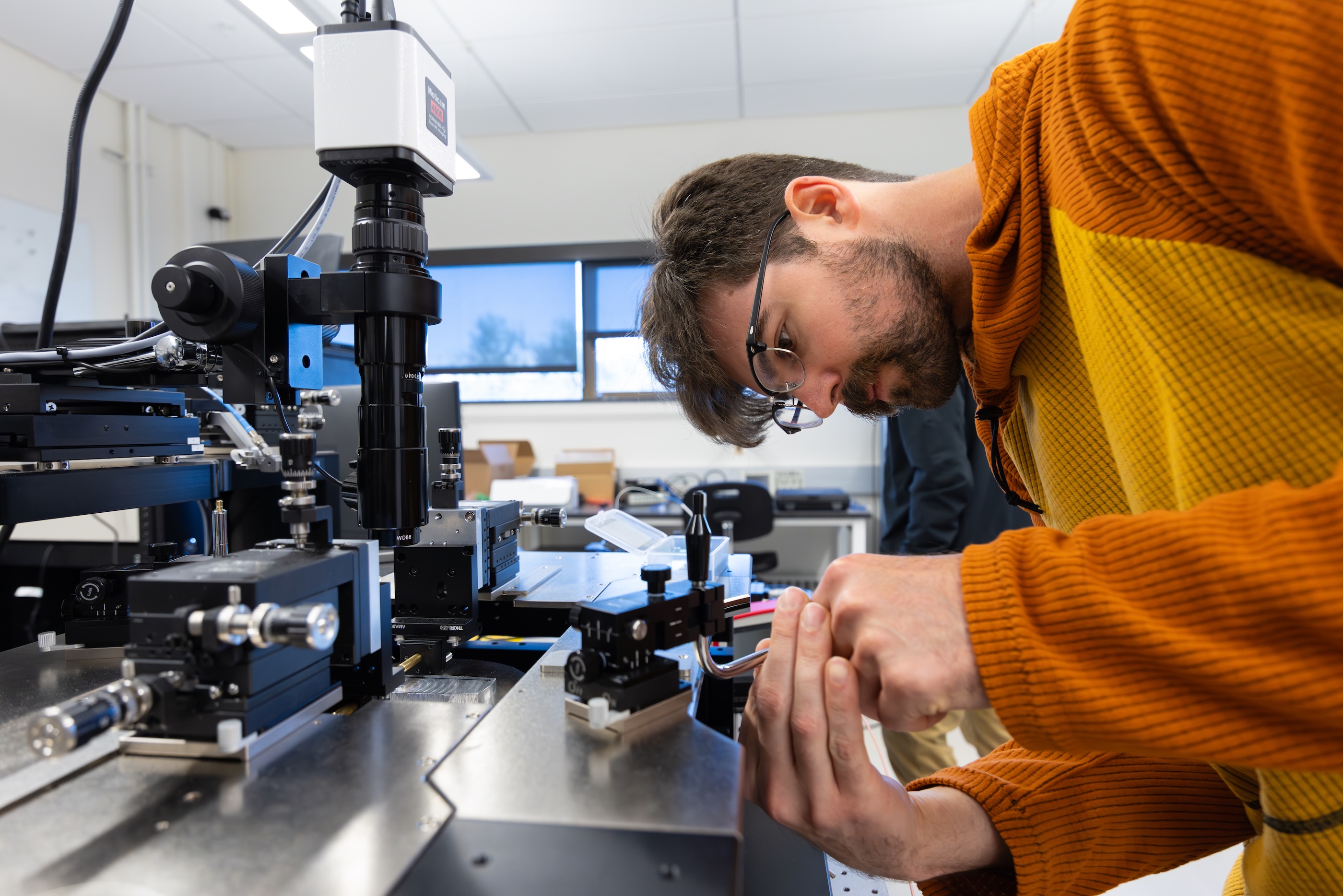 A Mines student in an orange sweatshirt aligns a microwave photonic chip in a lab on the Mines campus.