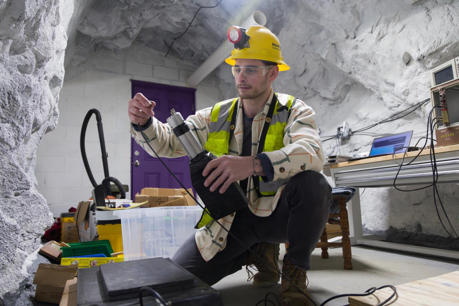 A student in a hard hat and safety glasses manipulates equipment in the Subatomic Particle Hideout in Edgar Mine.