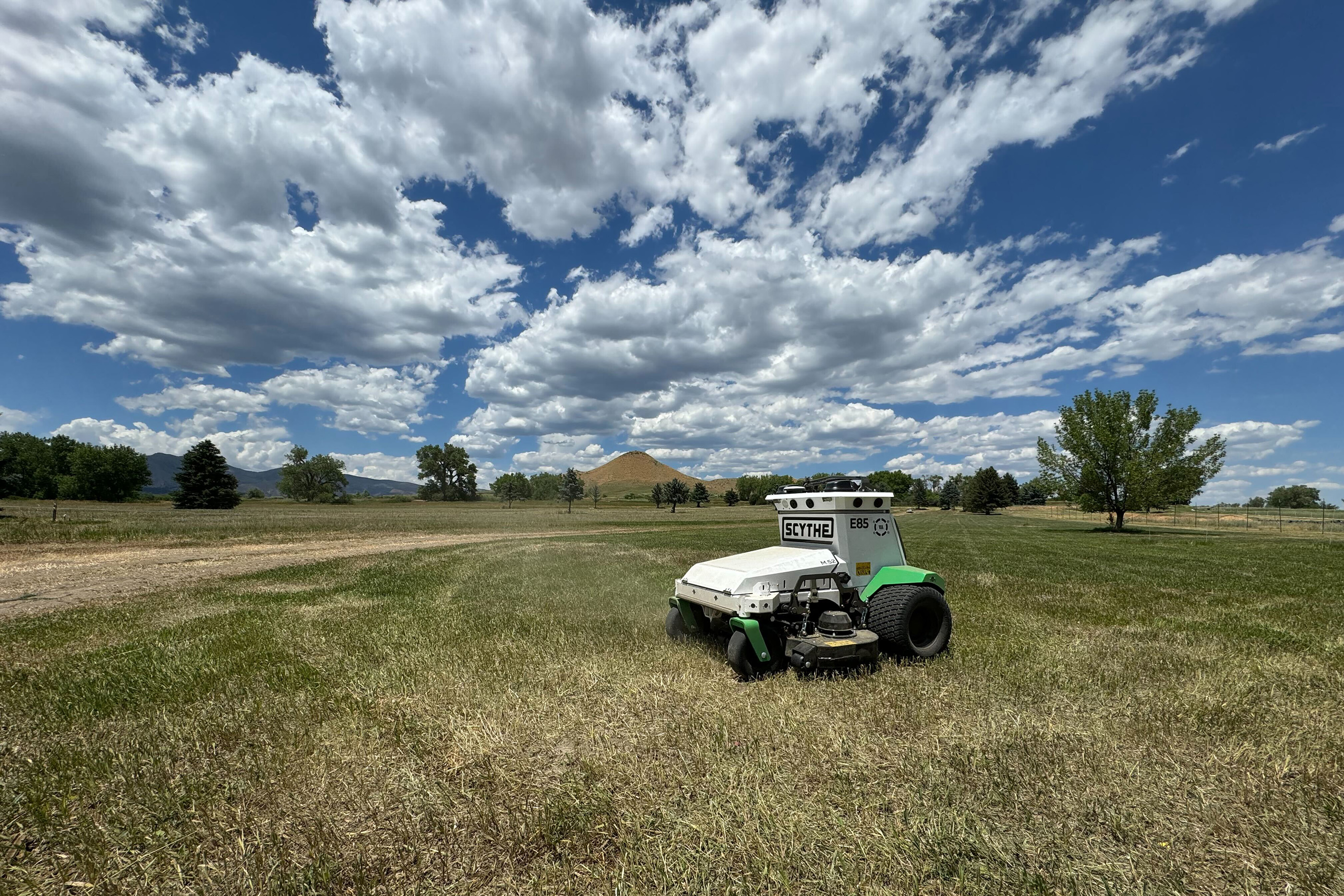 A lawn mowing robot in a field with a cloud filled blue sky above