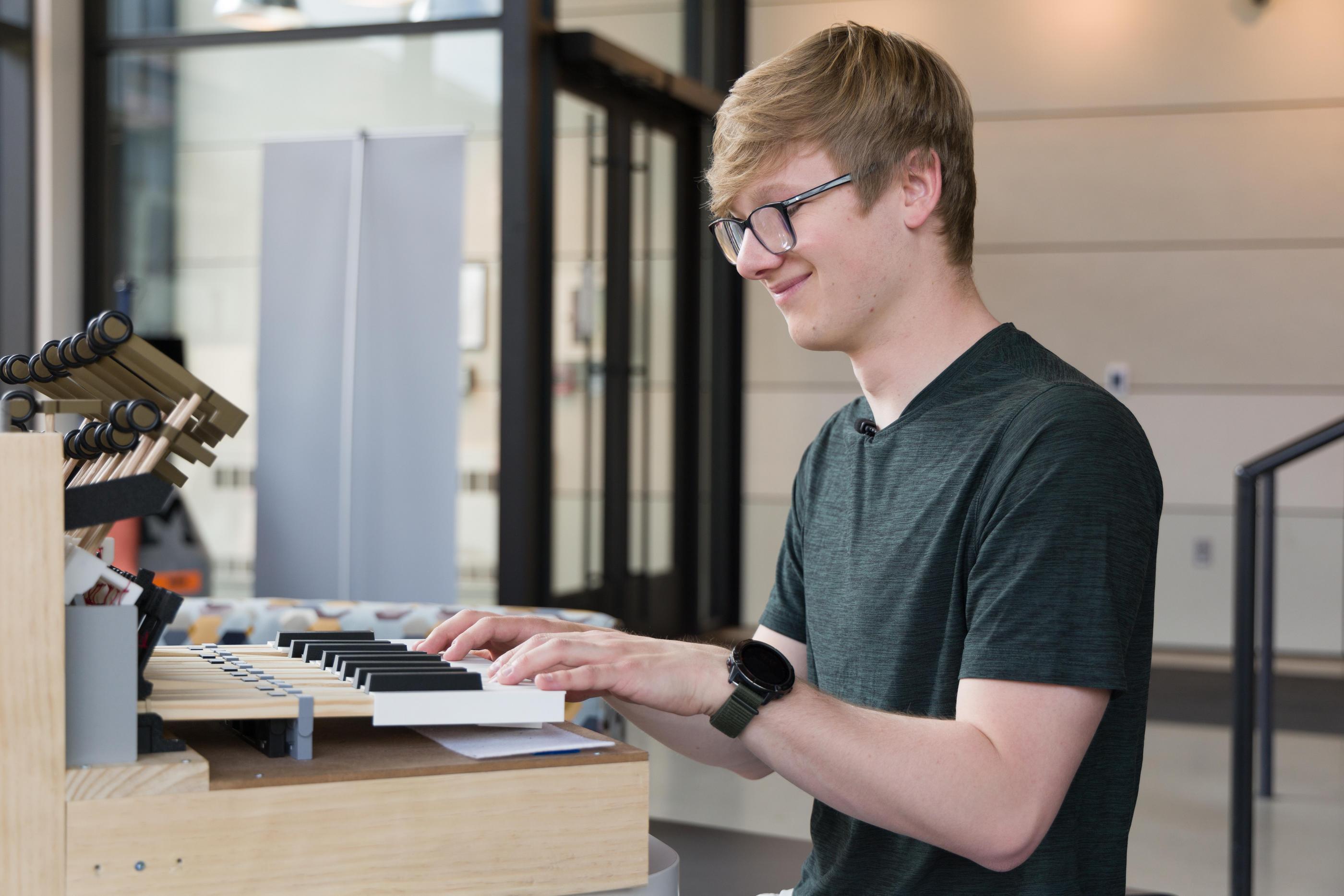 A student sits in front of a handmade instrument with his hands on piano keys