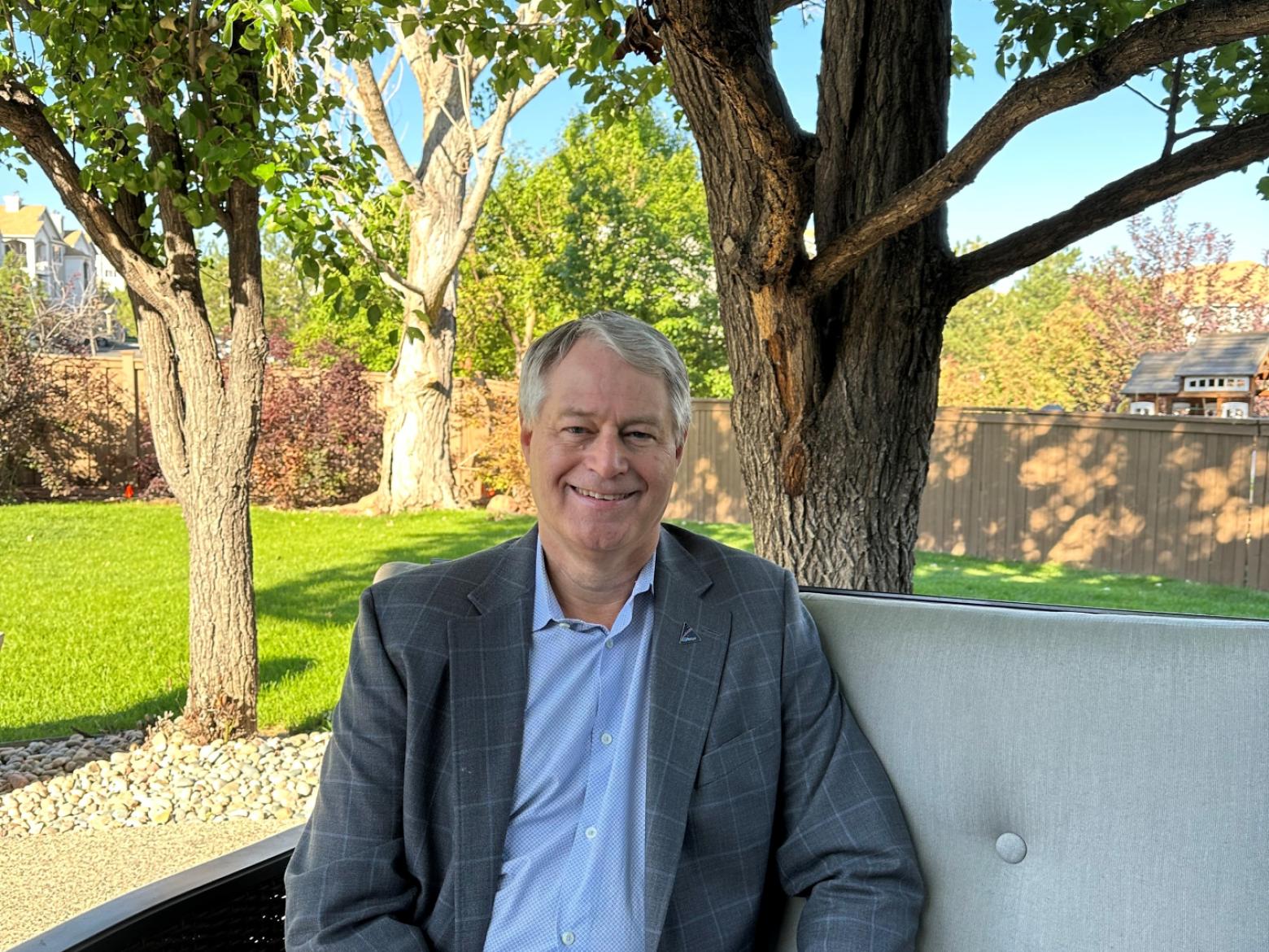 Mine alum Paul Anderson and rocket scientist for Lockheed Martin poses on outdoor seating with trees in the background.