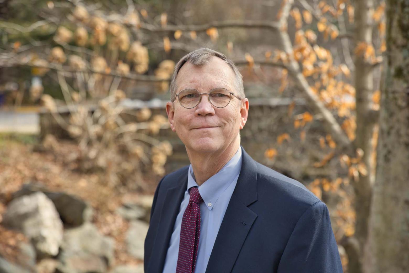 Jim Ashe headshot with fall trees blurred in the background