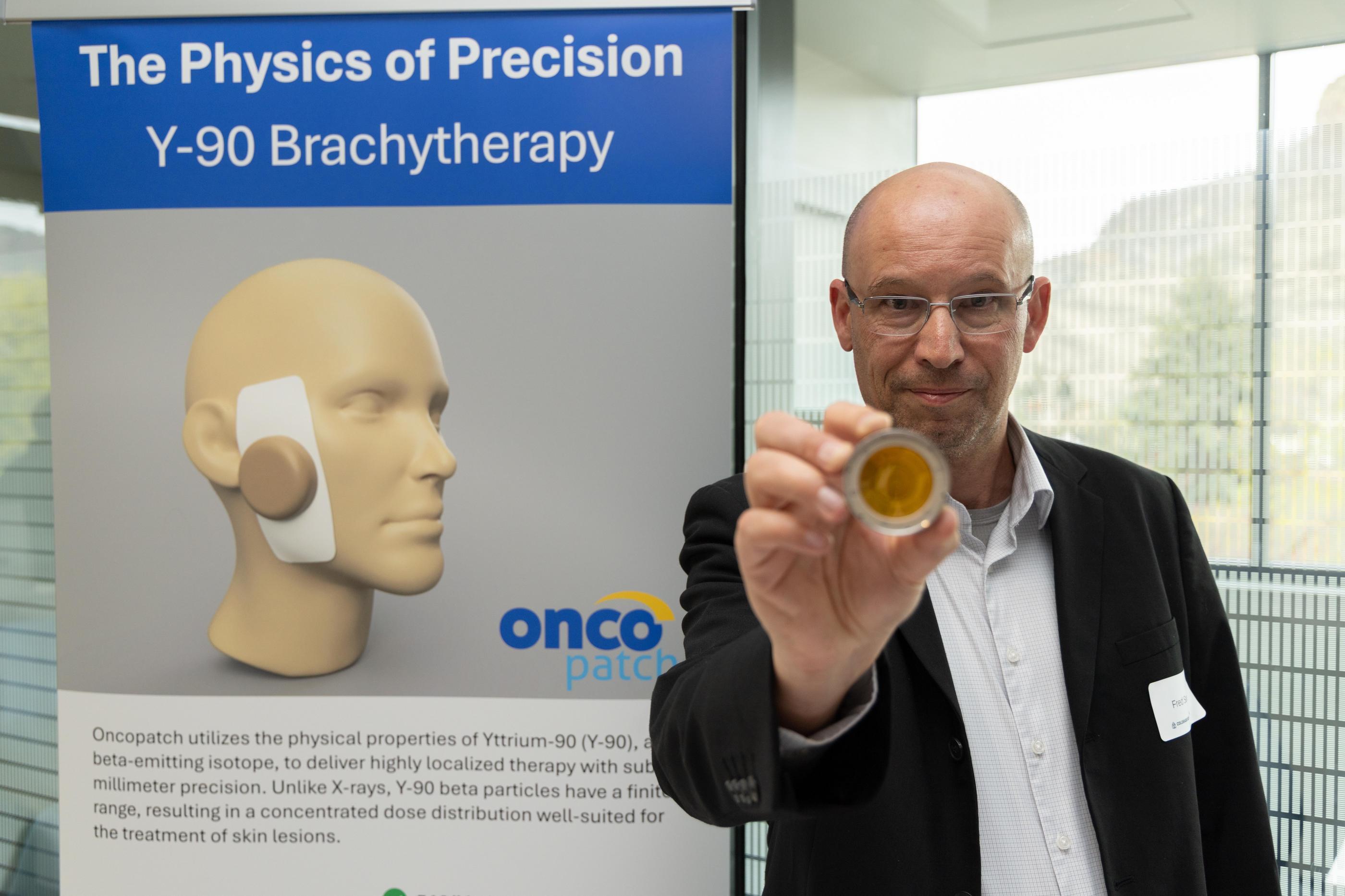 Fred Sarazin holds a demo OncoPatch in front of a pull-up banner explaining the technology