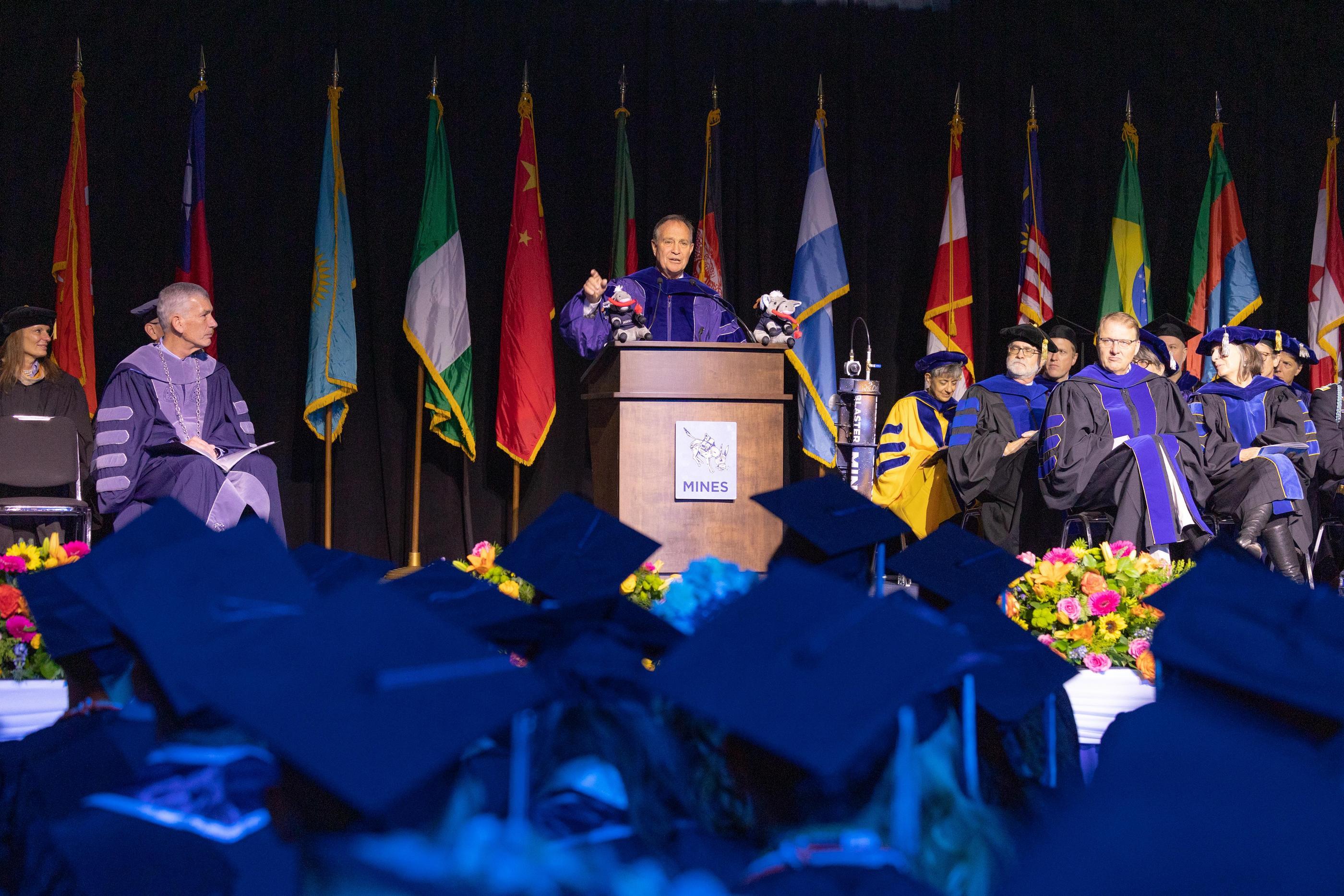 Ed Perlmutter stands behind the podium on the Mines commencement stage