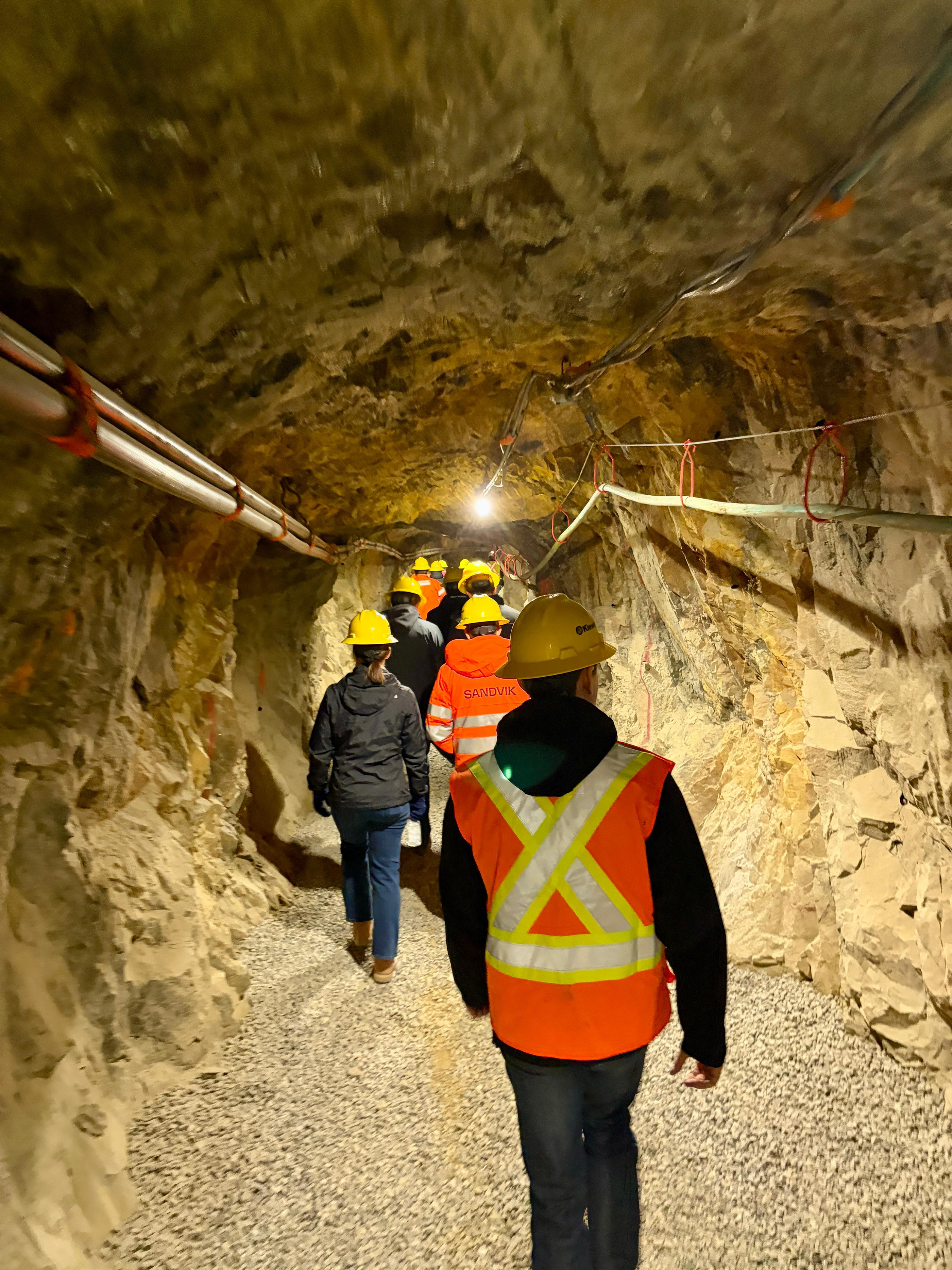A group of engineers in hard hats and reflective vests tour an underground mine