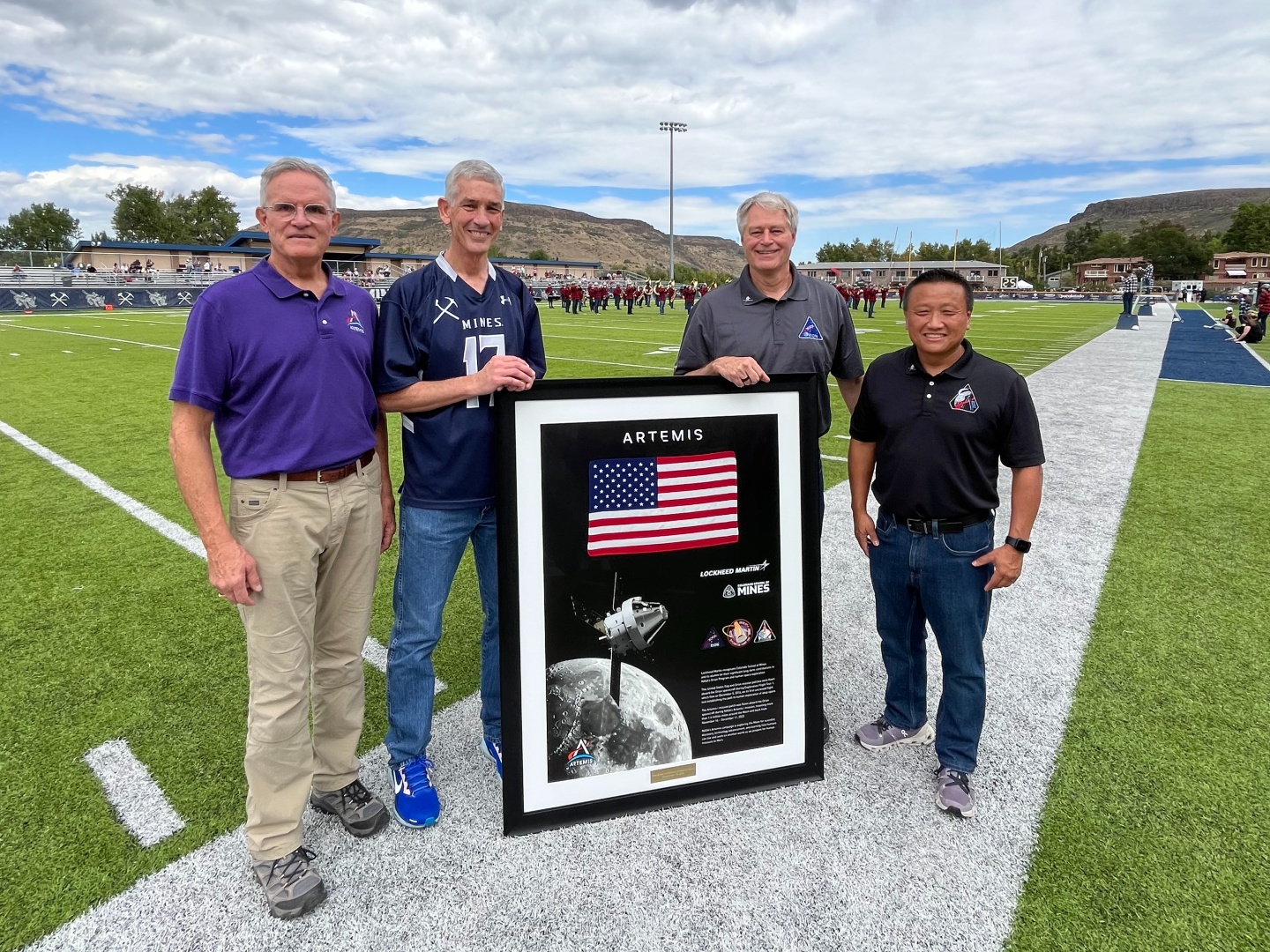 Lockheed Martin employees and alumni pose with Orion memorabilia on field at Marv Kay Stadium
